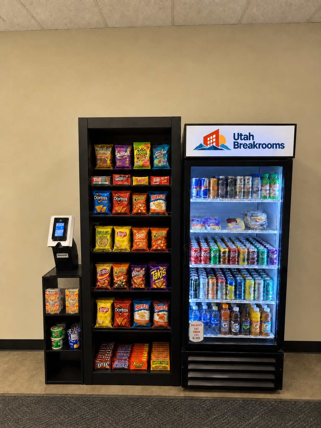 A Utah Breakrooms micro market with a self-checkout kiosk, an open snack rack, and a lit drink cooler topped with the Utah Breakrooms sign.